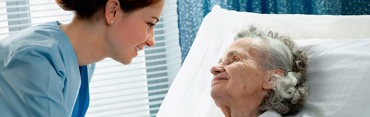 Pflegekraft mit älterer Dame am Krankenbett