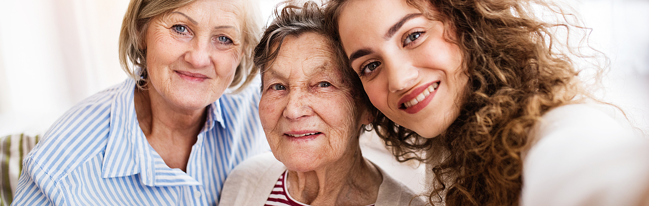 Drei Frauen mit unterschiedlichem Alter stehen eng zusammen