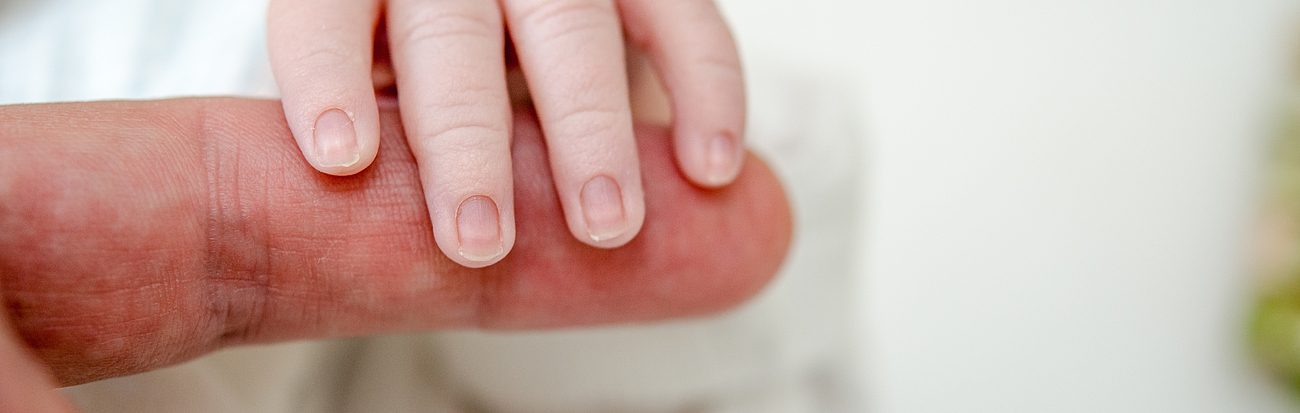 Hand eines Neugeborenen umschließt Finger einer erwachsenen Person