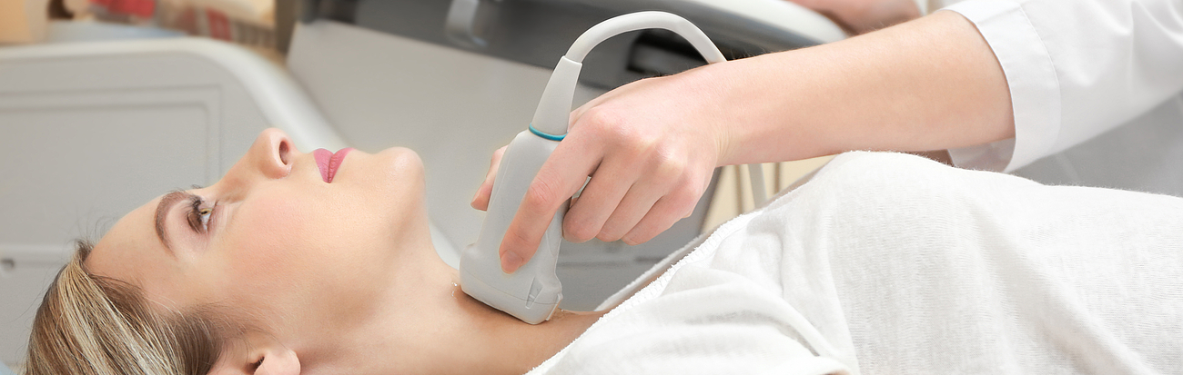 Eine Patientin liegt auf einer Liege und die Schilddrüse wird mithilfe von Ultraschall untersucht.